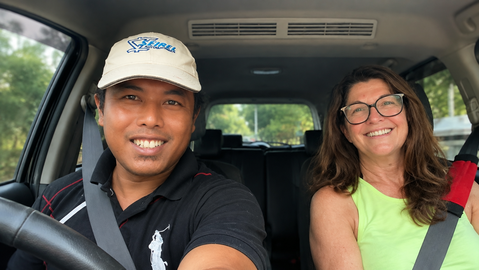 Smiling local driver and a happy guest in an air-conditioned car during a Bali transfer